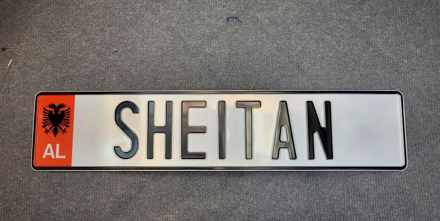 SHEITAN — biela tabuľka s albánskym pásikom AL a čiernym razeným písmom